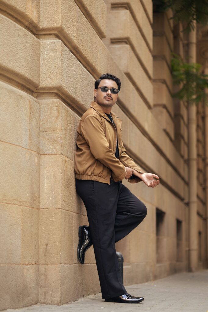 Stylish man in sunglasses leans against an urban building wall, exuding confidence and style.