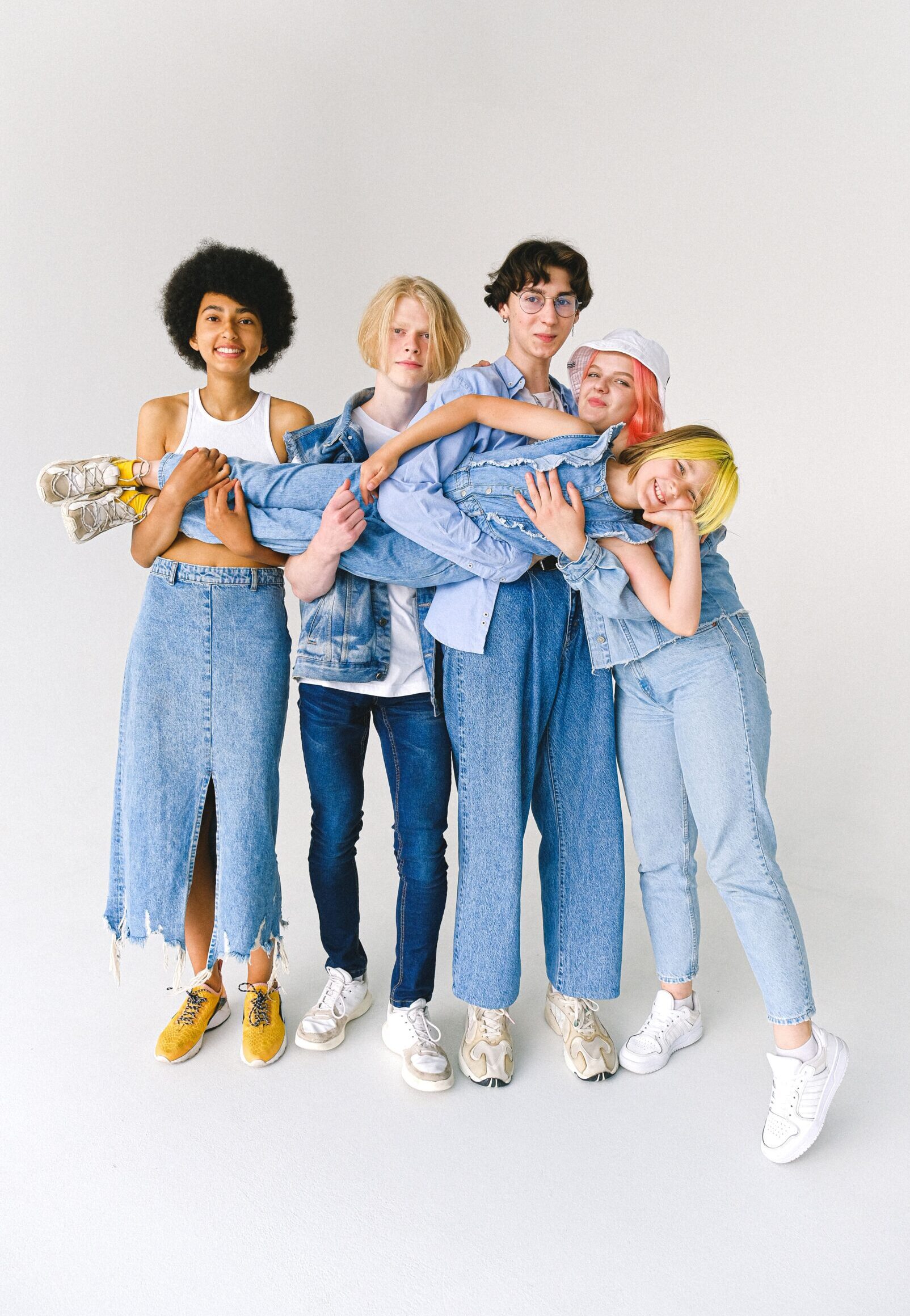 Full length of multiracial friends in casual clothes standing in studio while holding child on hands on white background while looking at camera