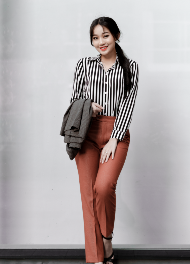 Asian woman in smart casual attire, smiling against a modern background.