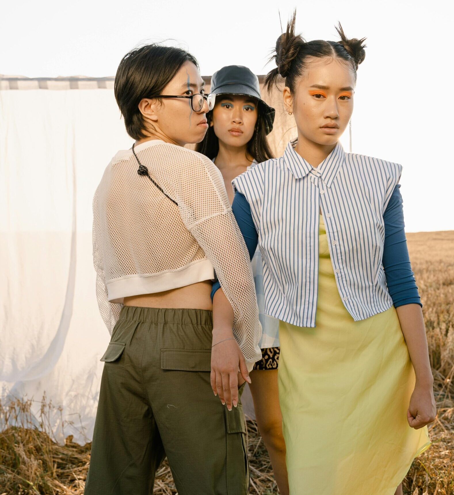 Three fashionable young women pose confidently in a vibrant outdoor setting, showcasing modern trends.