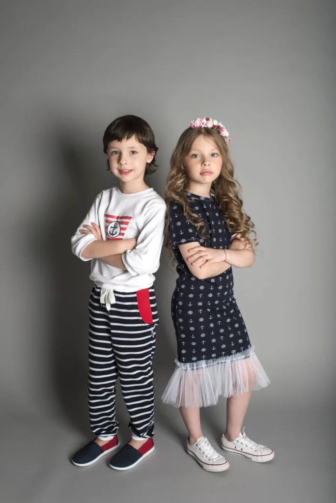Two children wearing stylish casual outfits, standing side by side with their arms crossed.