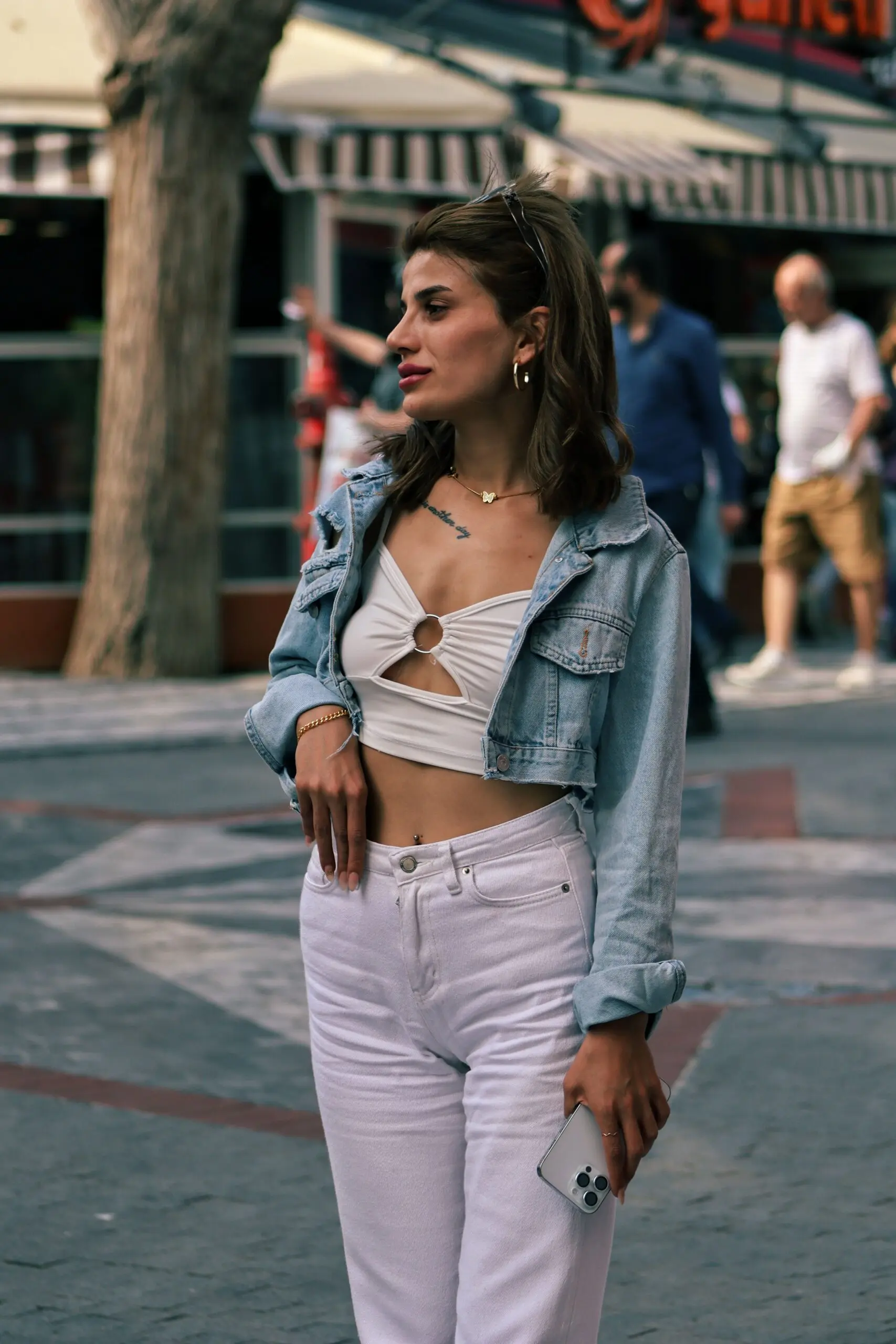 Woman wearing a white crop top, white jeans, and a blue denim jacket in a street fashion look.