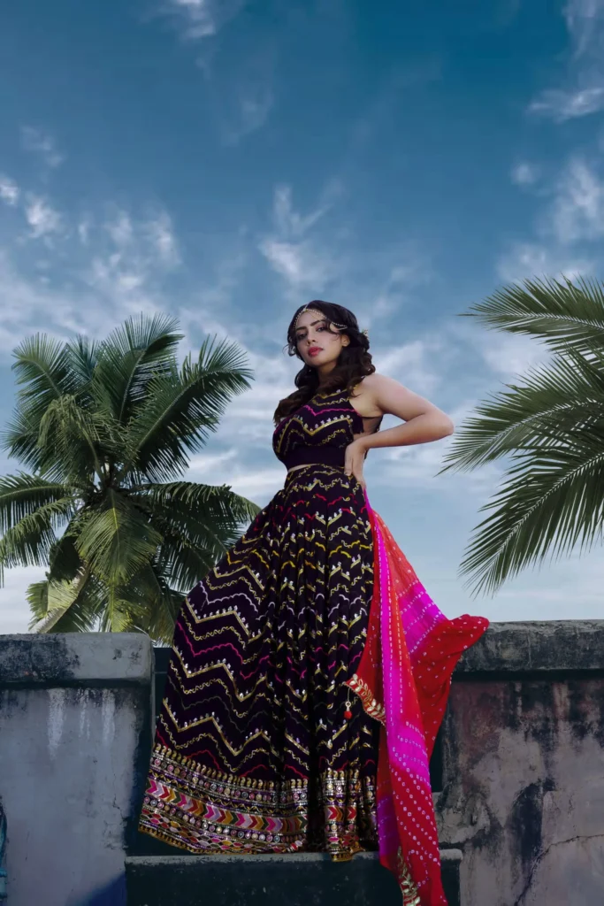 A stylish woman poses elegantly in a vibrant partywear dress outdoors with palm trees in the background.