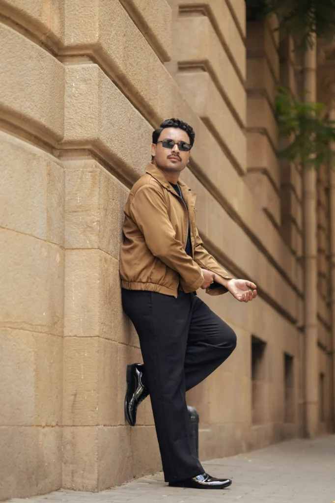 Stylish man in sunglasses and wearing black pant and jacket an urban building wall, exuding confidence and style.