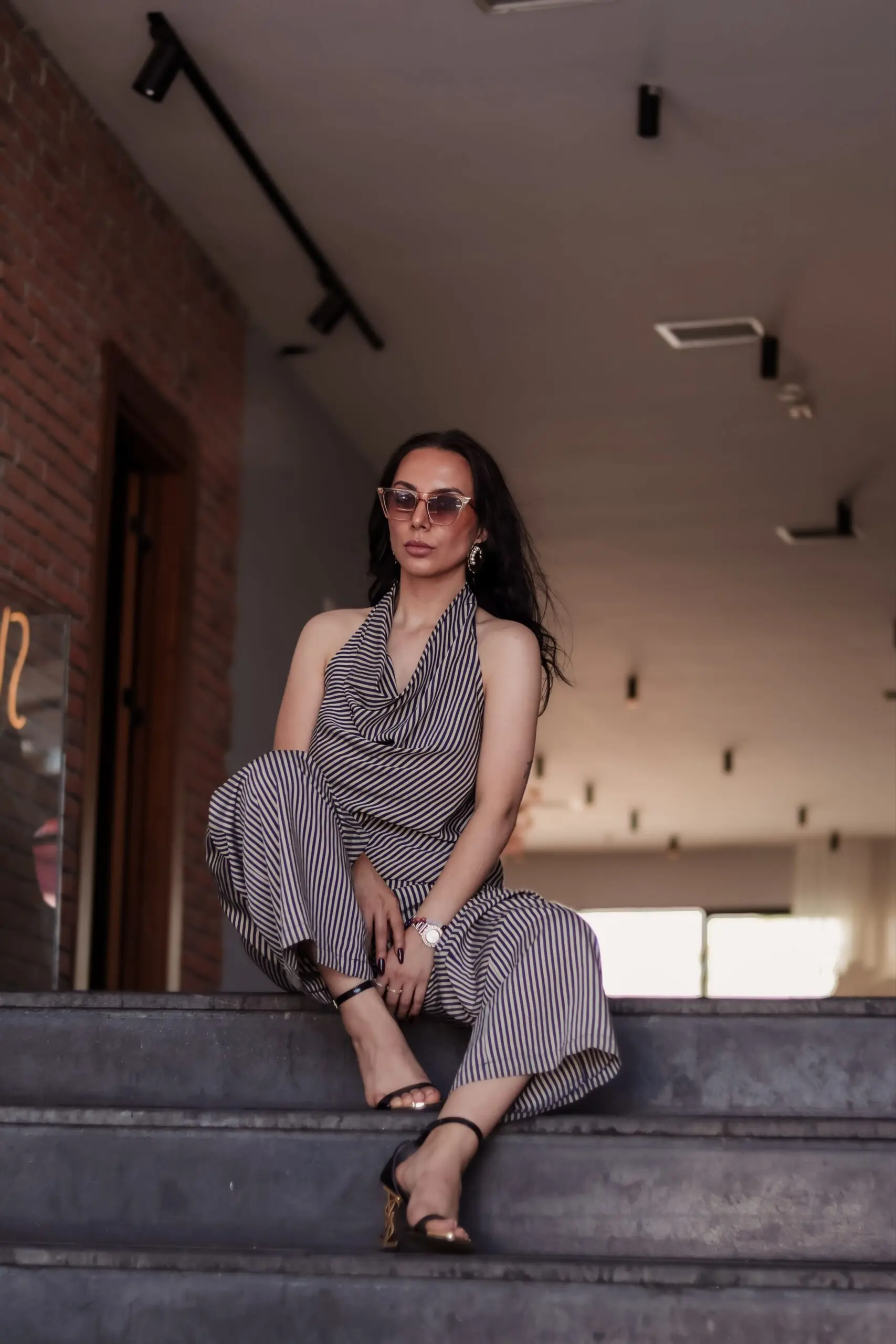 Women wearing a stylish grey jumpsuit sitting on stairs in a modern building.