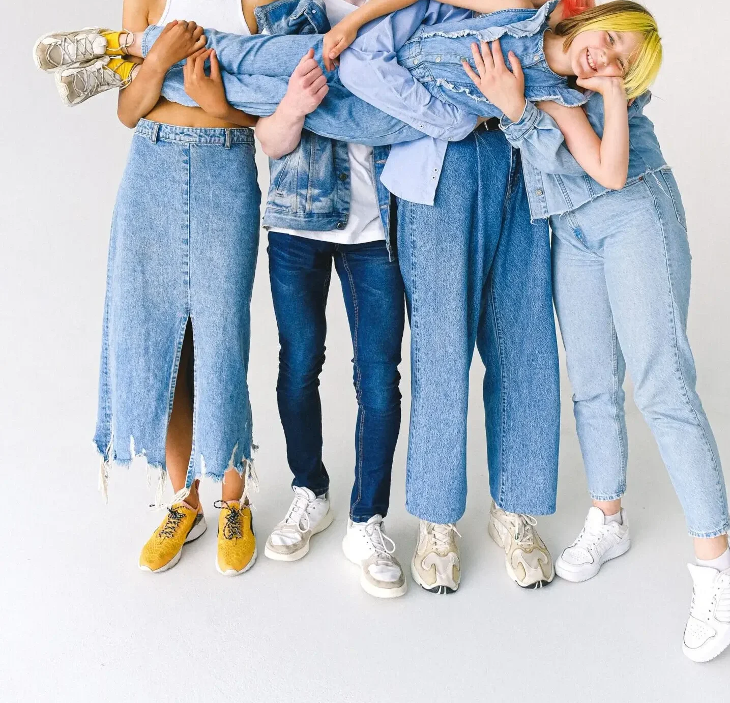 Full length of multiracial friends in casual clothes standing in studio while holding child on hands on white background while looking at camera.