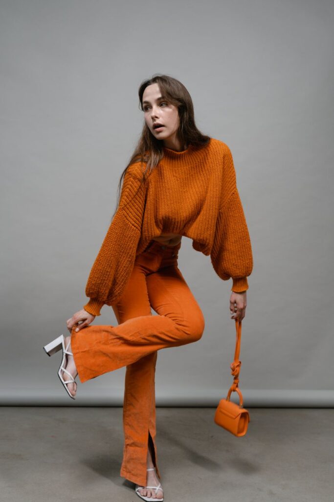 Stylish woman poses in a vibrant orange outfit and high heels in a studio setting.